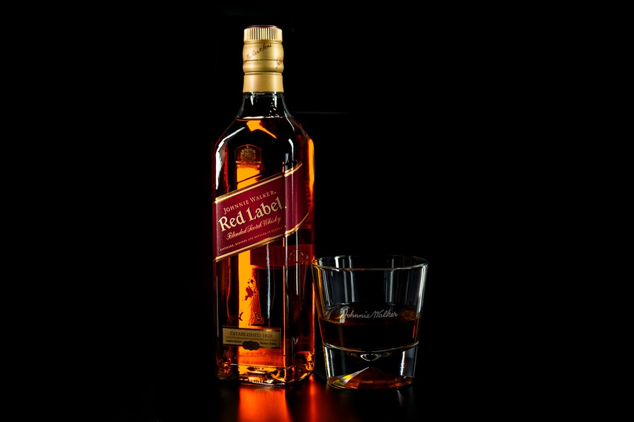 services-03 Close-up of a whiskey bottle and glass on a dark background, highlighting the amber color and glossy reflection.