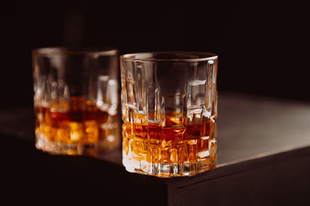 services-04 Crystal glasses filled with whiskey on a dark wooden surface, highlighting texture and color.