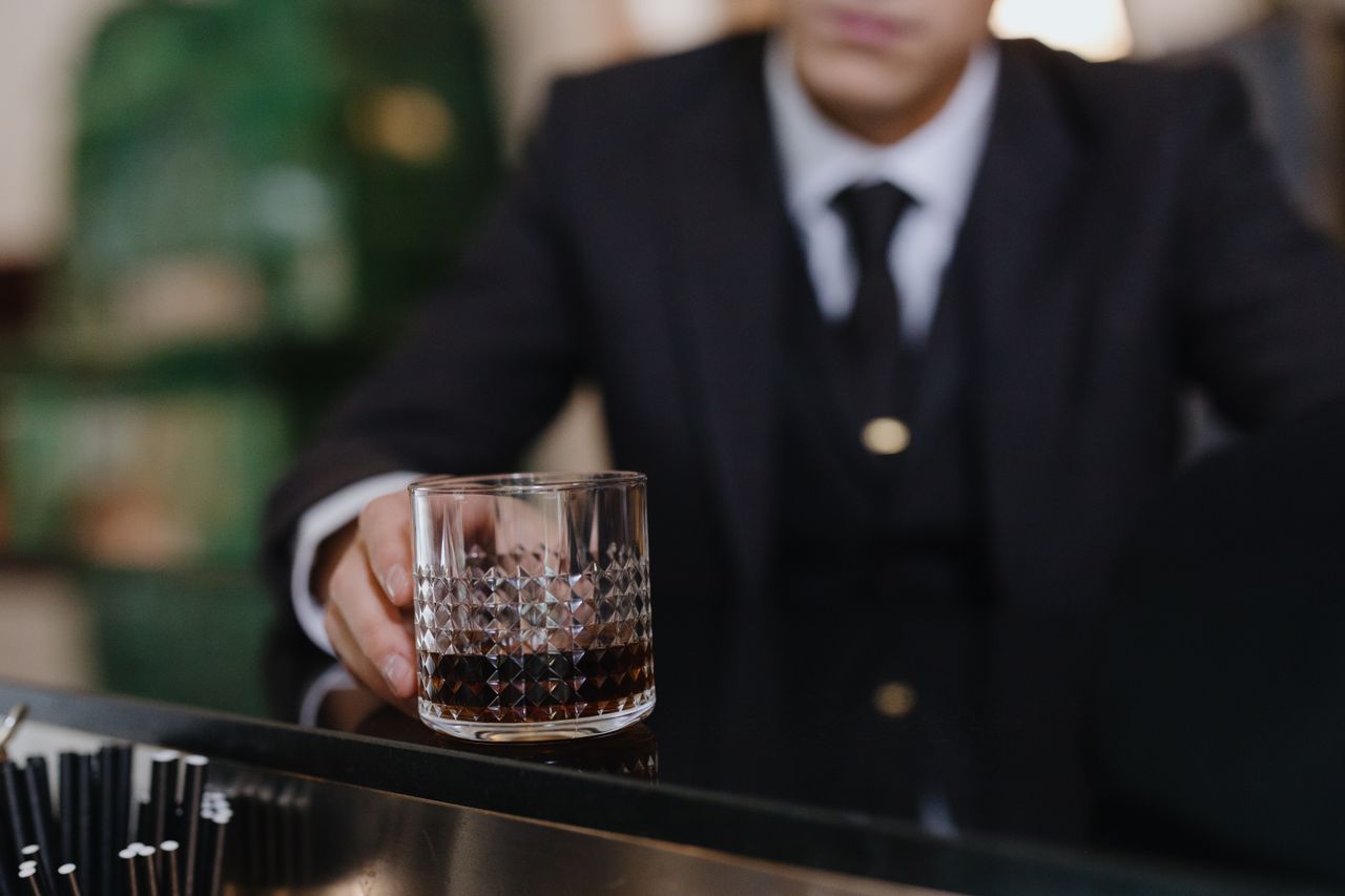 Close-up of a man in a suit holding a glass of whiskey at the bar counter.